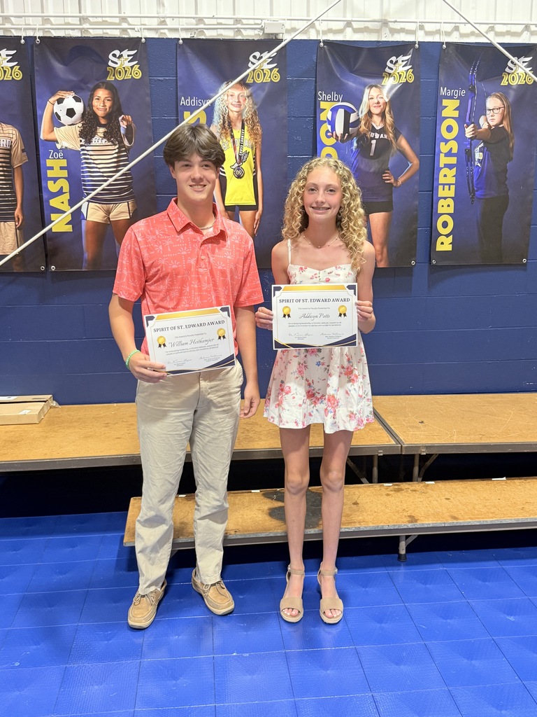 Two 8th grade students stand on stage holding Spirit of St. Edward Award certificates.