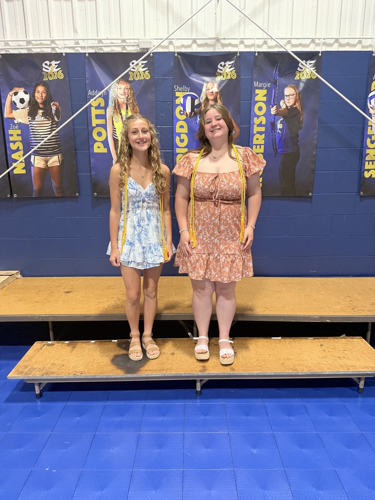 Two 8th grade students stand on stage wearing honor cords during the Awards Breakfast ceremony.