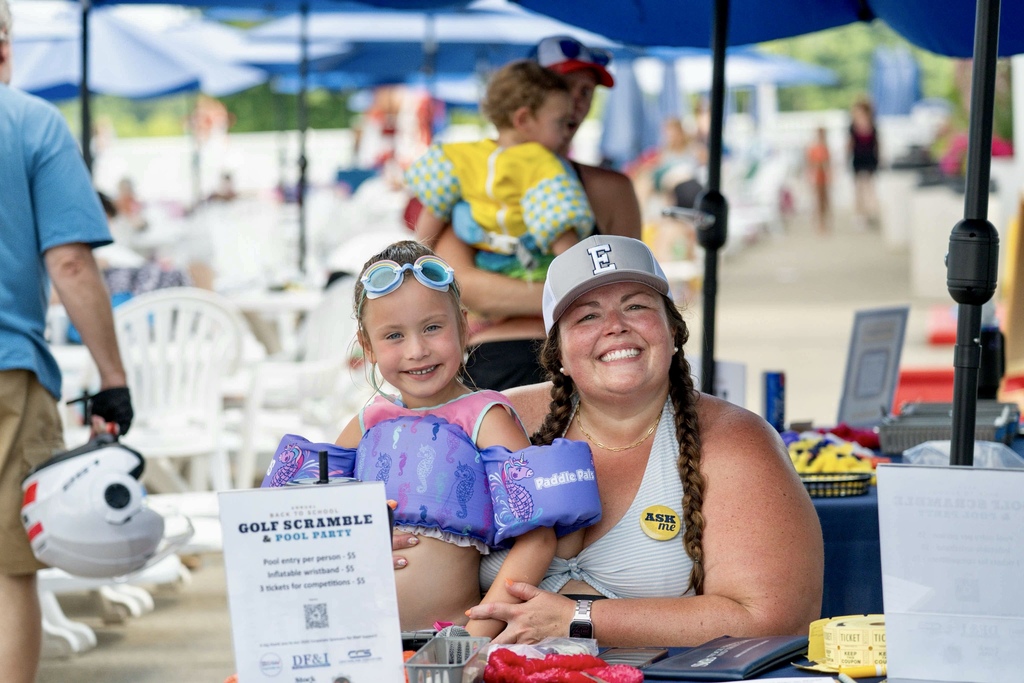 Students sit together around a table during a summer pool party, smiling while playing Bingo and enjoying time with classmates.