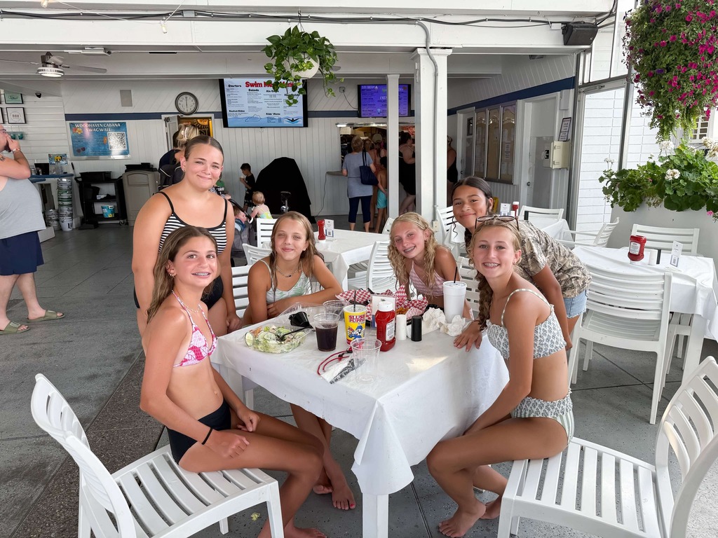 Students sit together around a table during a summer pool party, smiling while playing Bingo and enjoying time with classmates.