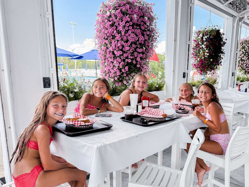 Students sit together around a table during a summer pool party, smiling while playing Bingo and enjoying time with classmates.