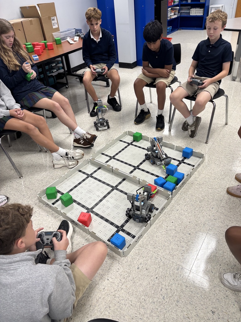 Students practice operating VEX robots on a classroom competition field while working together during a 7th grade STEM robotics activity.