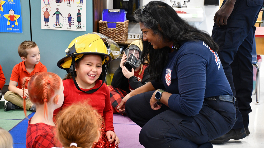 girl smiling with firefighter helmet on and firefighter smiling