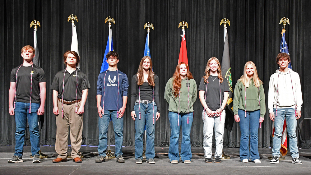 eight students on stage with military flags behind them