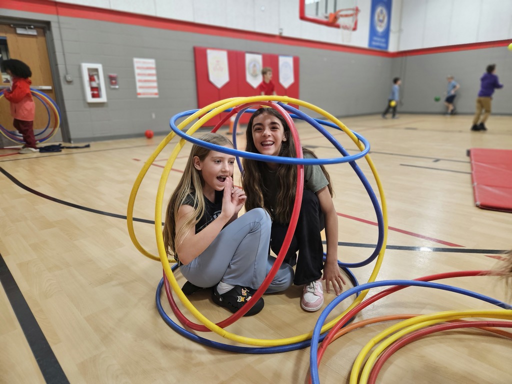 Two students sit inside a sphere made of hula hoops. 