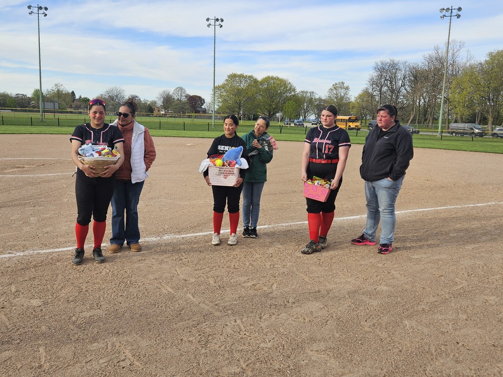Senior softball players are on the field holding gift baskets with a parent. 