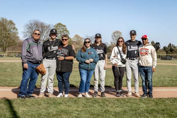 Senior Night baseball with 3 players and their parents standing on foul line