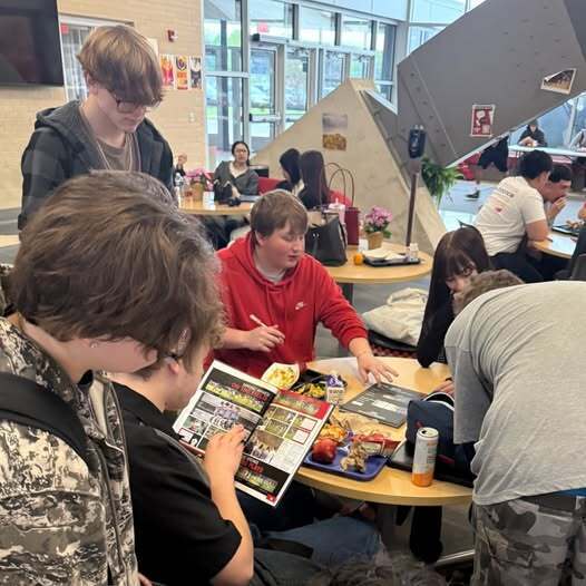 Students in cafeteria signing yearbooks at a table during lunch