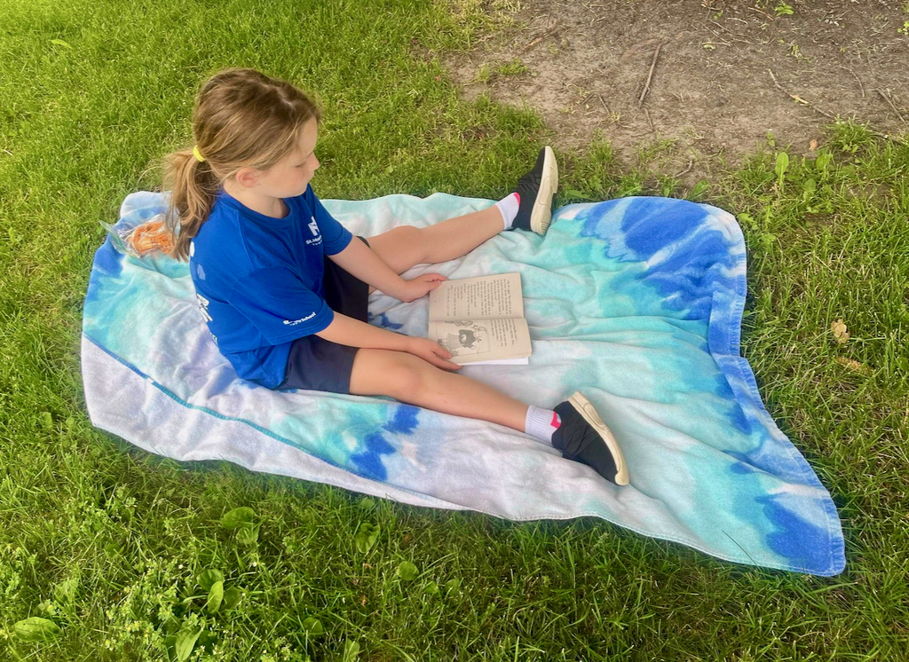 students reading books outside on blankets in the grass