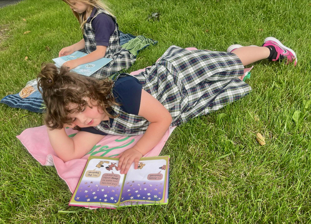 students reading books outside on blankets in the grass