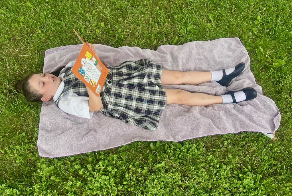 students reading books outside on blankets in the grass
