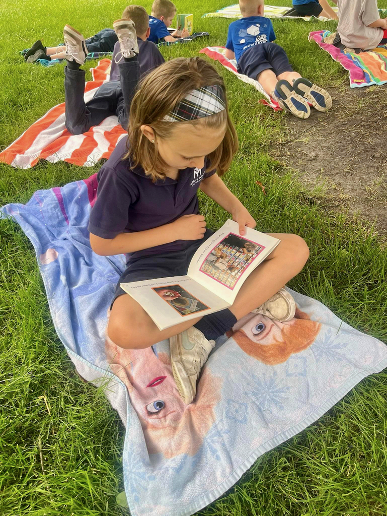 students reading books outside on blankets in the grass