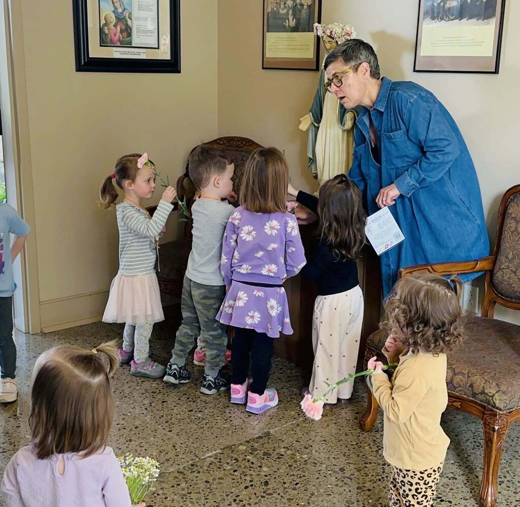 children putting flowers by a mary statue