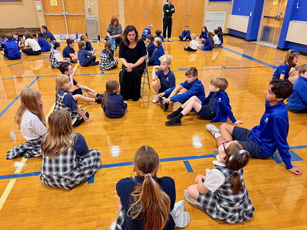 group of students sitting in a cirlce on a gymnasium floor with their teacher