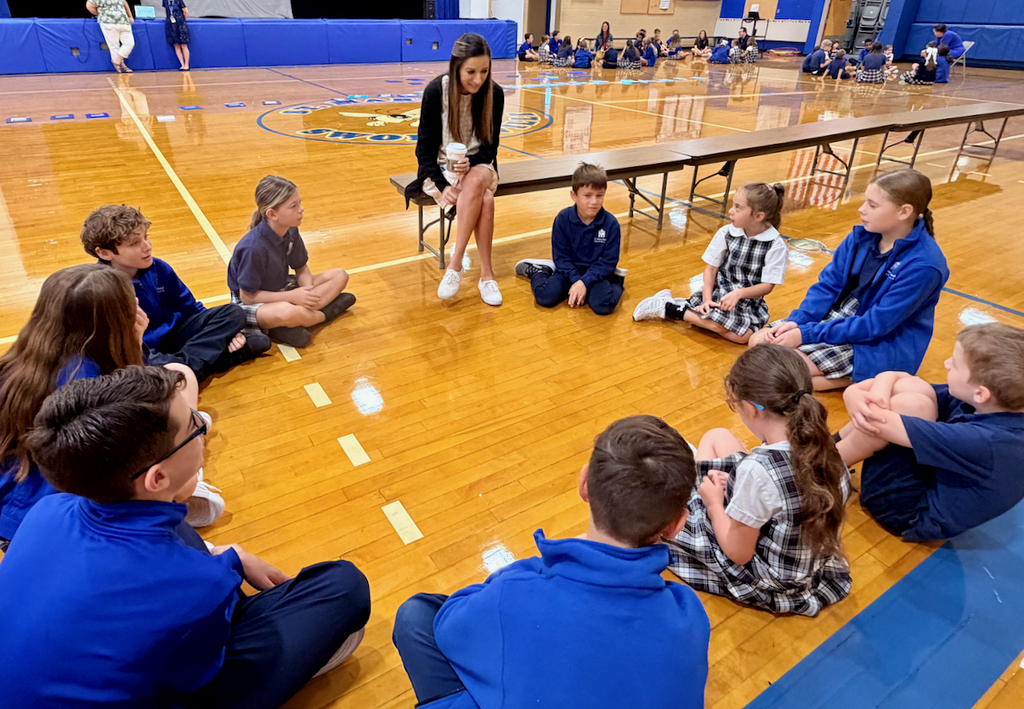 group of students sitting in a cirlce on a gymnasium floor with their teacher