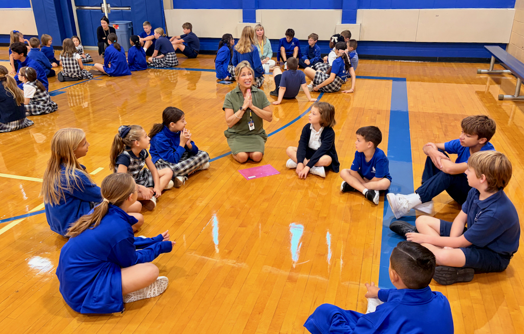 group of students sitting in a cirlce on a gymnasium floor with their teacher