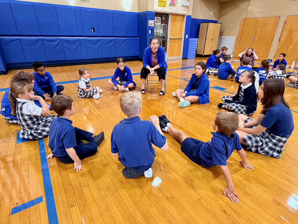 group of students sitting in a cirlce on a gymnasium floor with their teacher