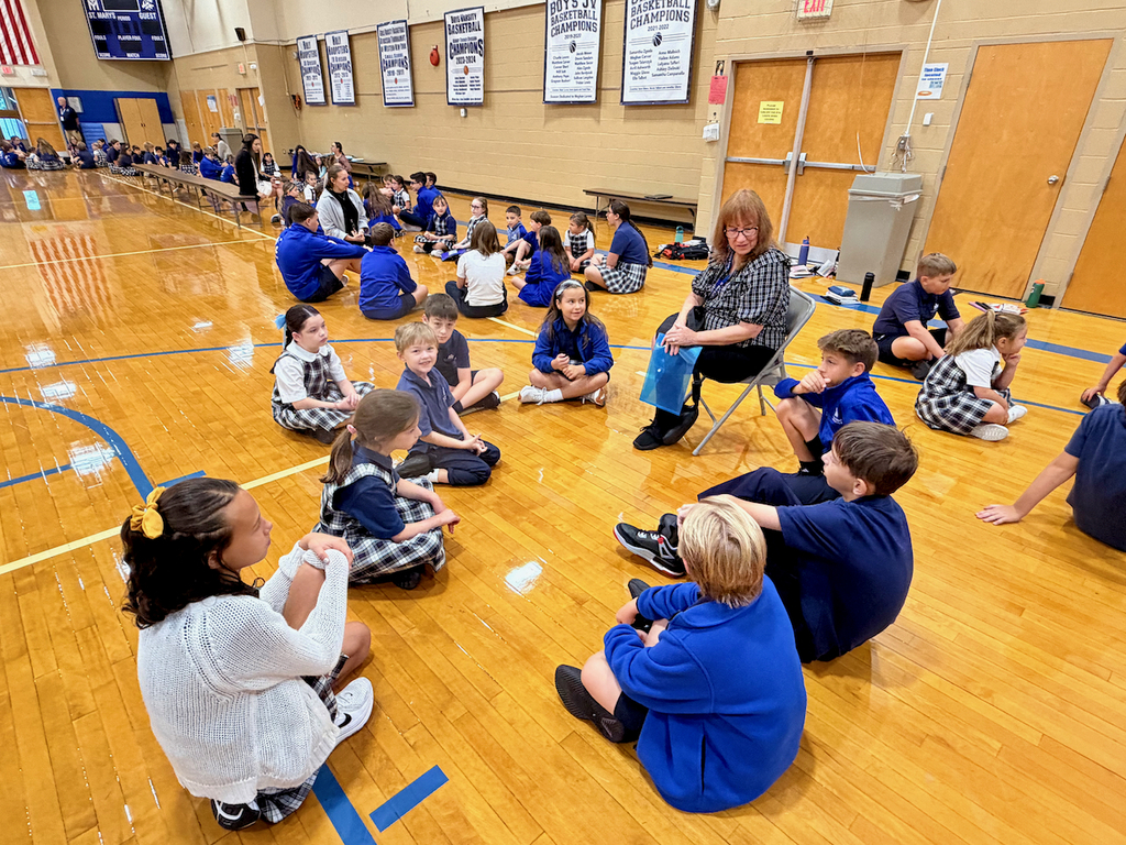 group of students sitting in a cirlce on a gymnasium floor with their teacher