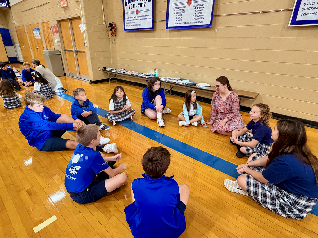 group of students sitting in a cirlce on a gymnasium floor with their teacher