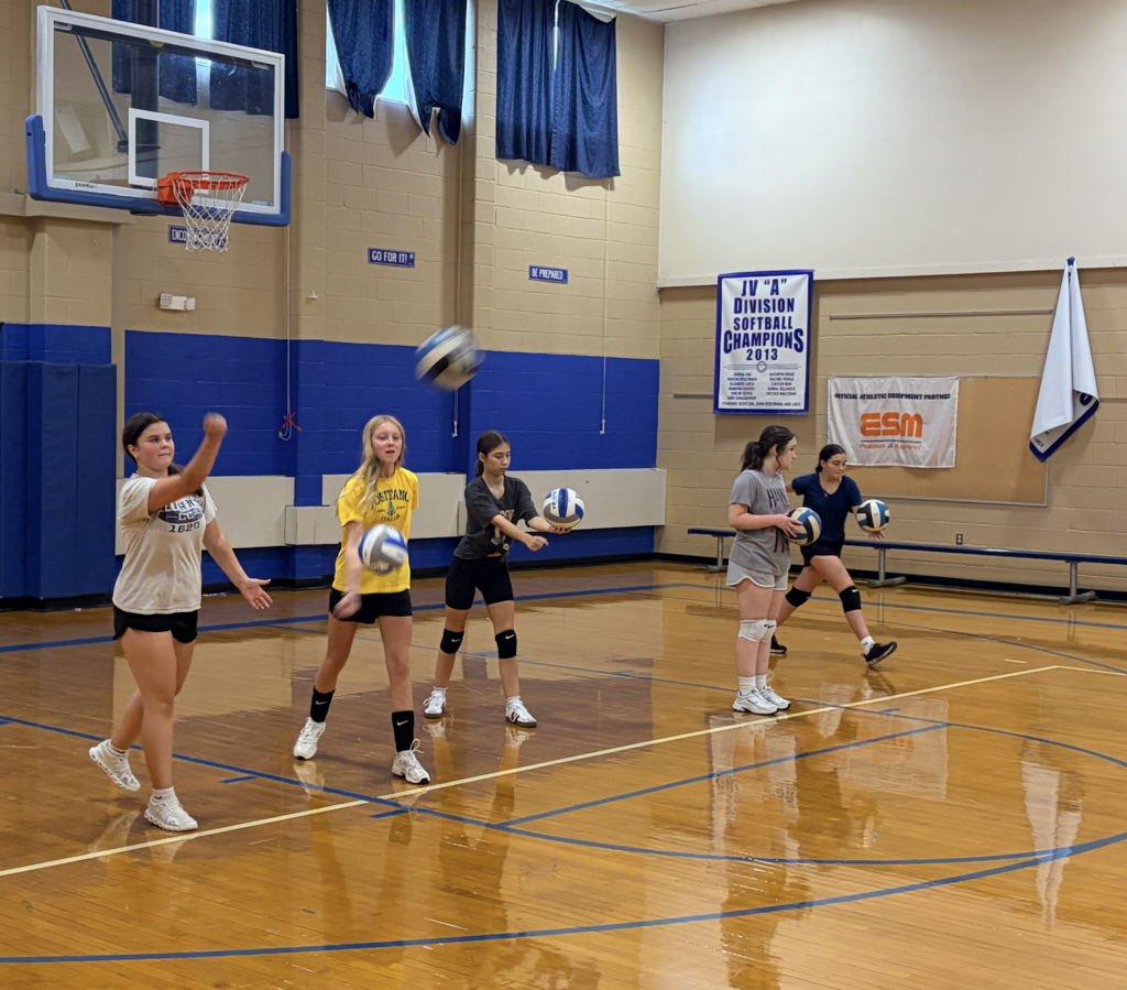 girls learning to serve volleyballs in gym