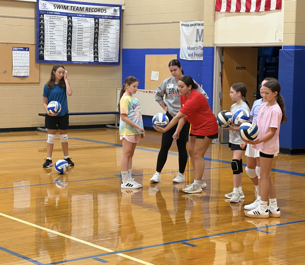 girls learning to serve volleyballs in gym