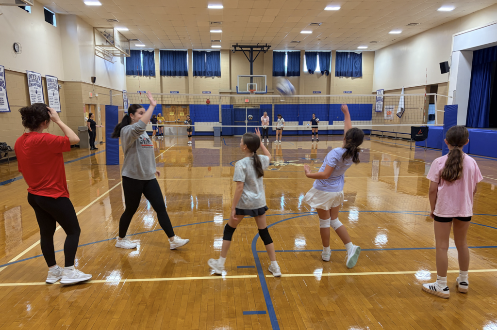 girls learning to serve volleyballs in gym