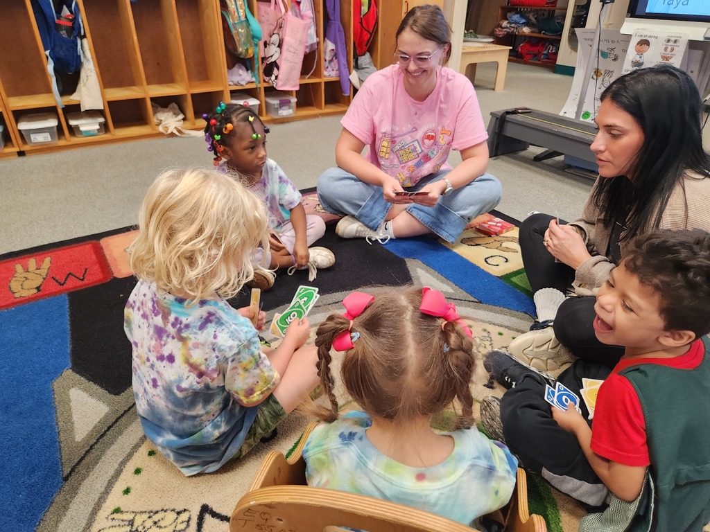 picture of 4 students and 2 teachers sitting in a circle on the floor playing uno.