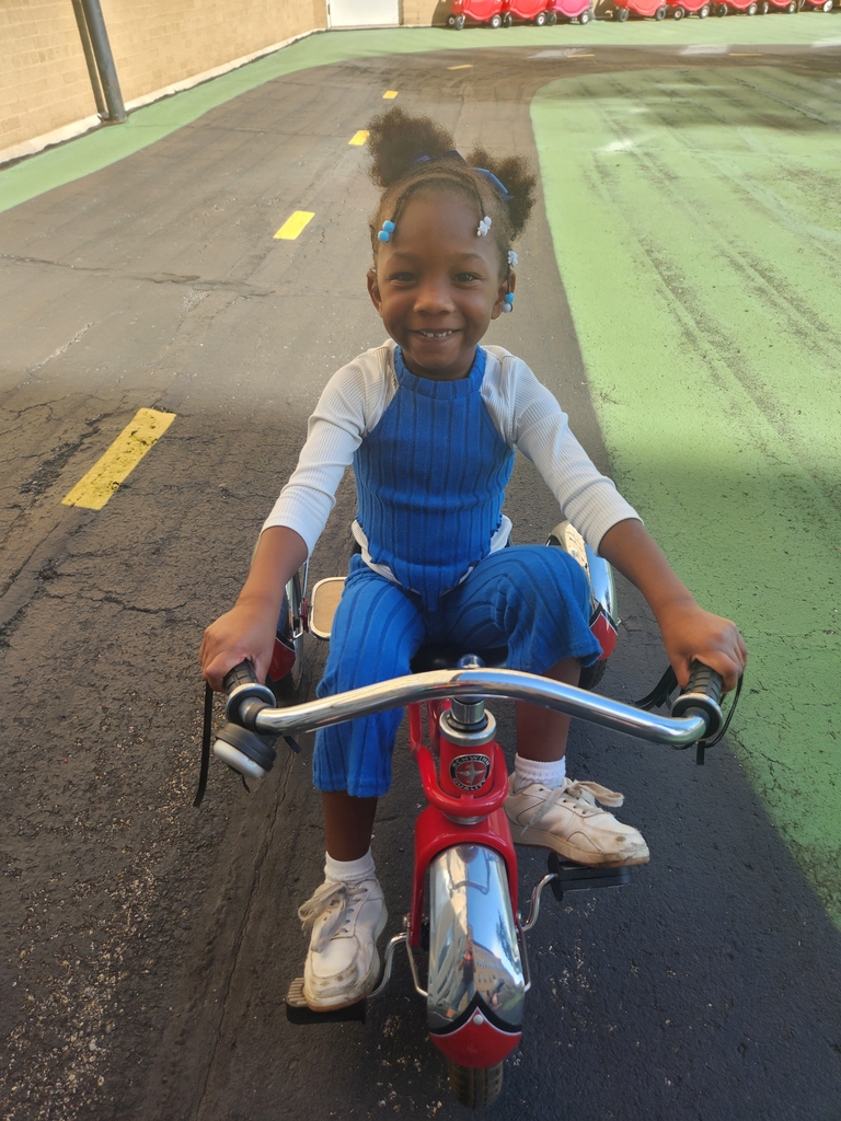 A student girl smiling while sitting on a red and silver tricycle.