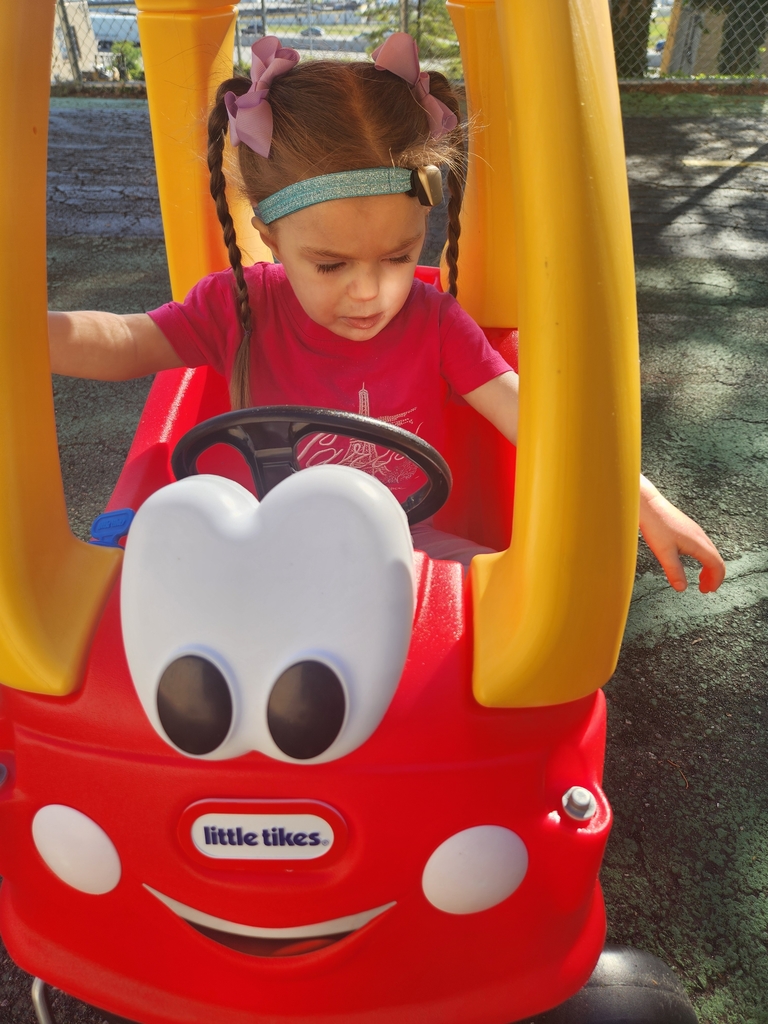 A student girl sitting in a red and yellow little tykes car