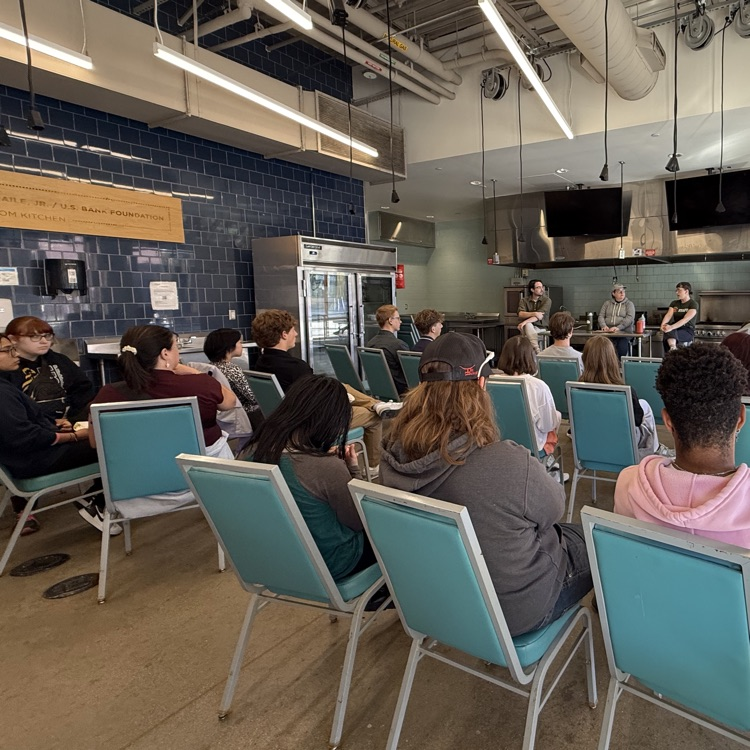 Students sit in a teaching kitchen listening to a panel of speakers share about culinary careers.