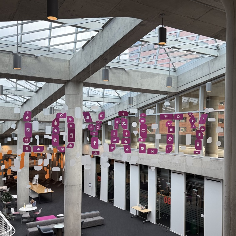 The photo shows the bright, modern interior of 84.51°, featuring open workspaces, glass walls, and colorful hanging displays spelling “LOYALTY.”