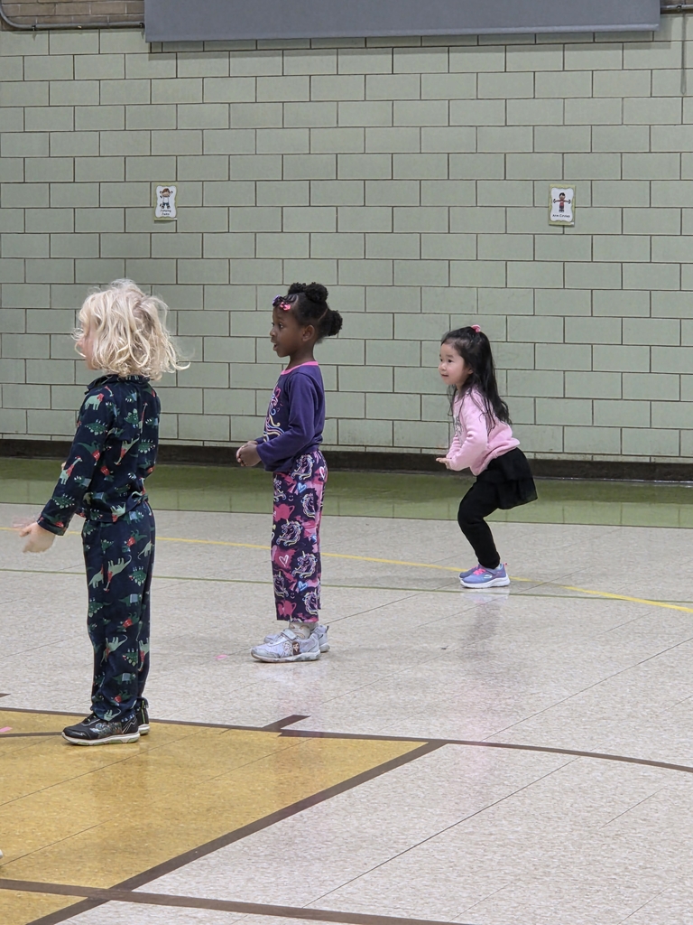 In the gymnasium 3 students are standing in a line. One student is dancing and the other 2 are standing still.
