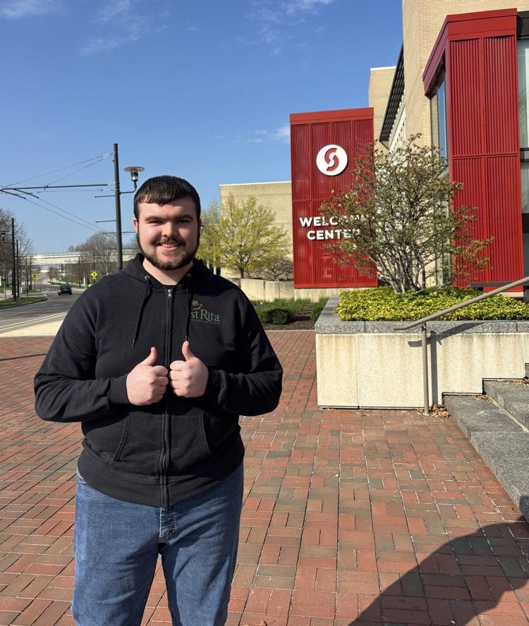 student standing behind Sinclair sign with a smile on his face and thumbs up. 