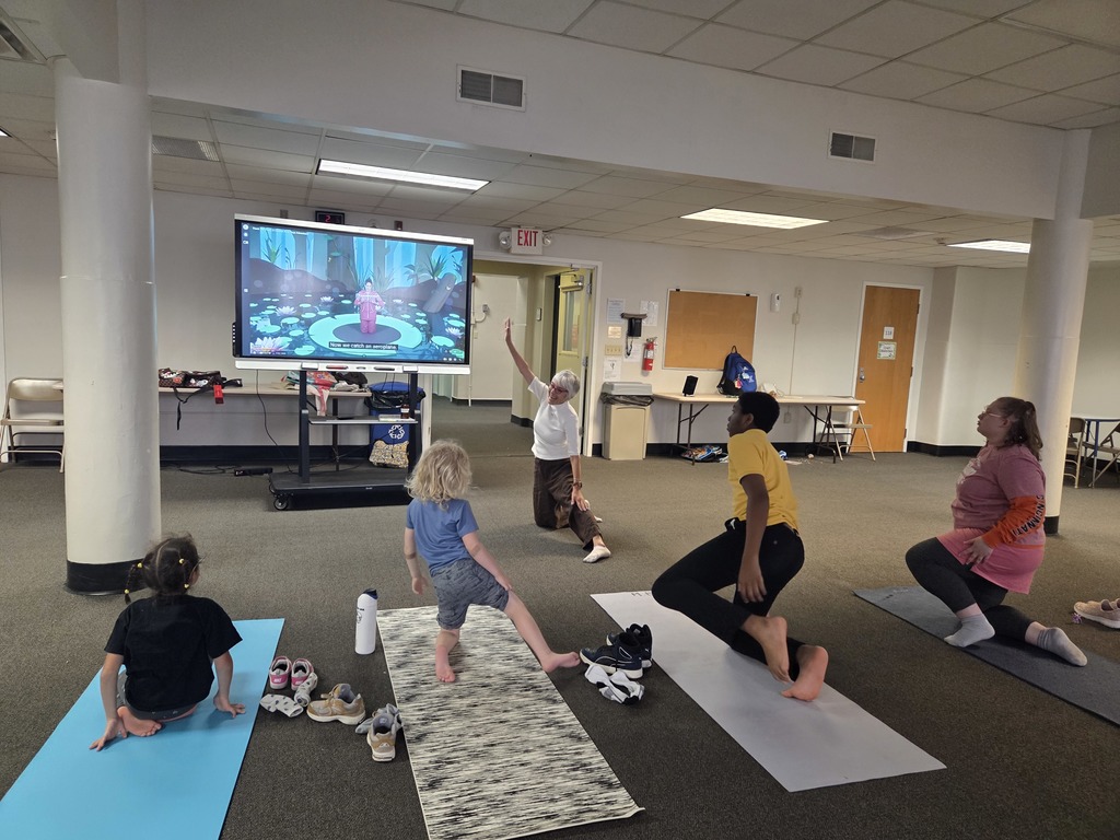 1 teacher and 4 students looking at the smartboard and copying the knee yoga pose. 
