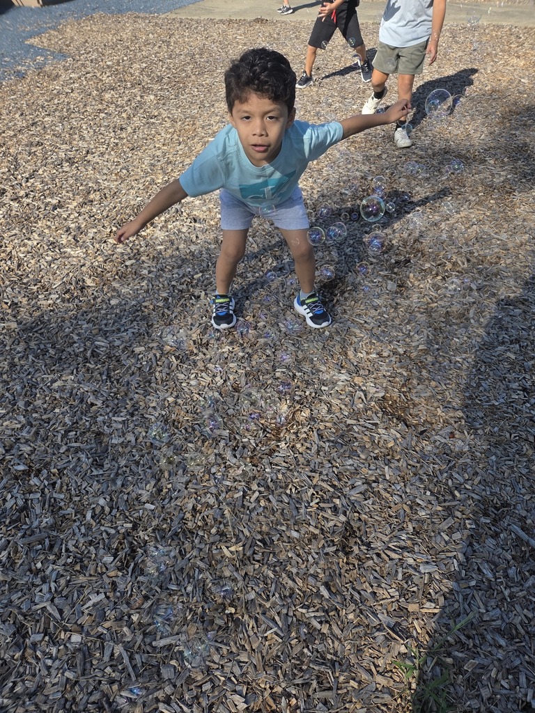 Picture: student leaning forward on mulch popping bubbles smiling.