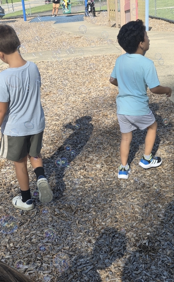 Picture: two students running on the mulch popping bubbles. Backs are towards the camera.