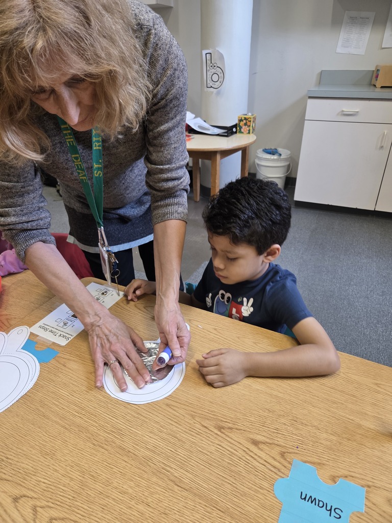Picture: teacher standing next to student helping them glue their mirror together.