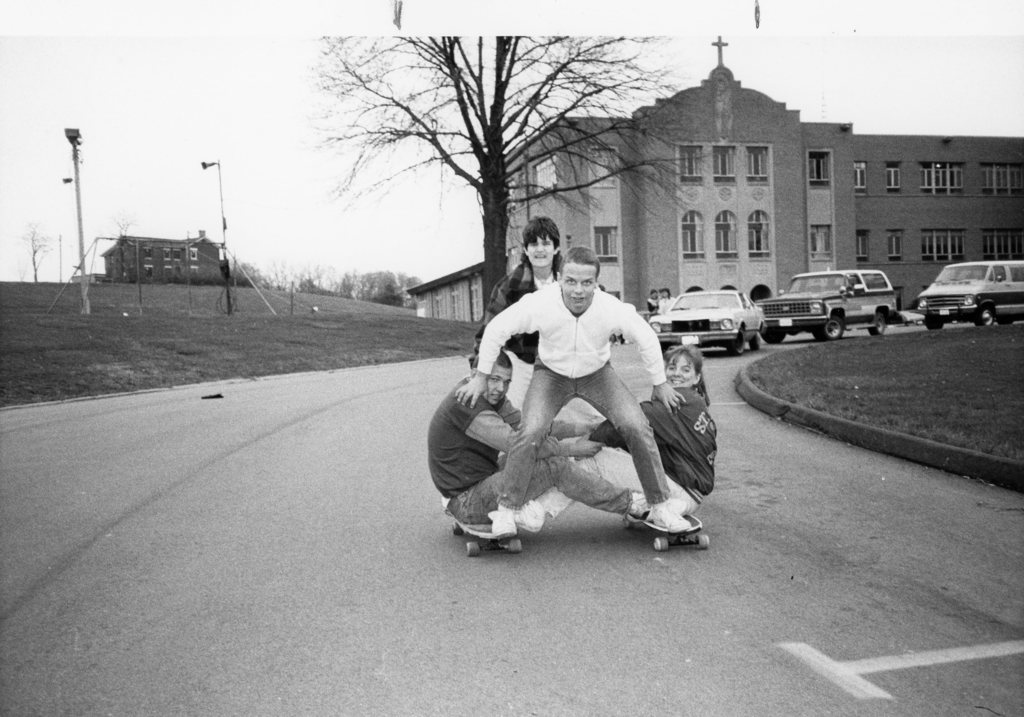 4 students on the skateboards outside front of school.