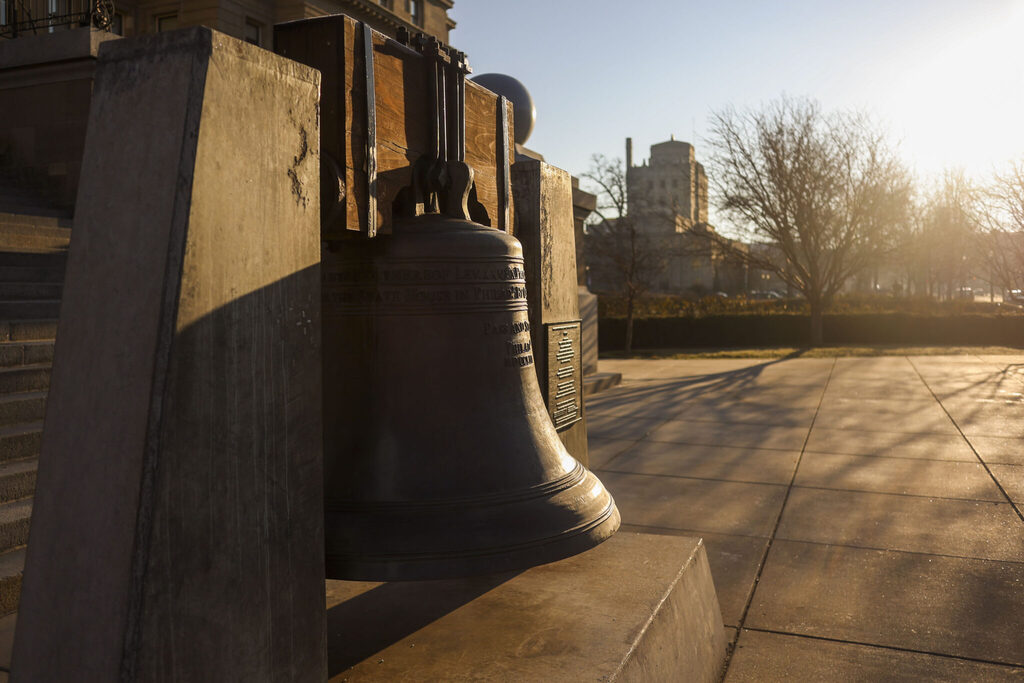 Replica Liberty Bell displayed outdoors in warm sunlight near the Idaho State Capitol.