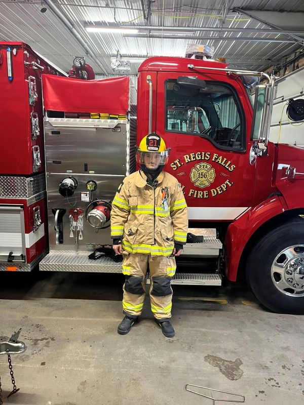 Male high school student with firefighter gear in front of a fire truck