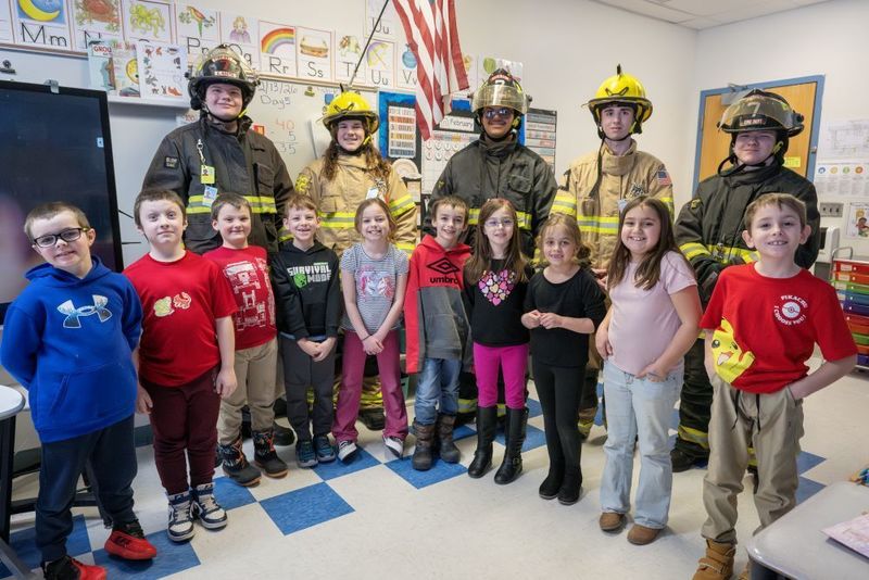 Small group of male high school students in firefighting gear with small group of elementary students