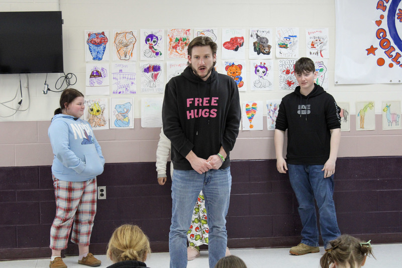 An adult male wearing a black sweatshirt with a young female student and older male student