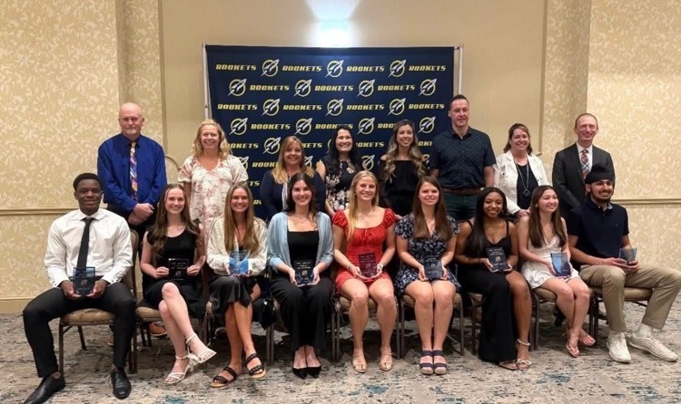 students standing and sitting in front of a banner that had the rockets logo 