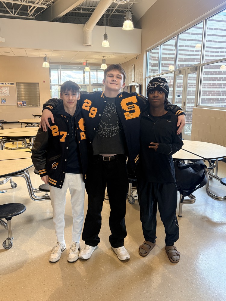 Three streetsboro wrestlers standing in a cafeteria. The student on the left and the the one in the middle are wearing letterman jackets.