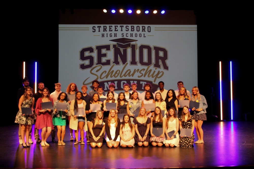 Seniors  stand on stage in front of a scholarship banner