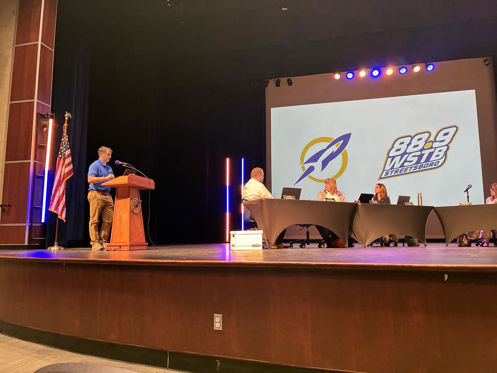 WSTB General Manager Corey presenting on stage at the March School Board of Education Meeting