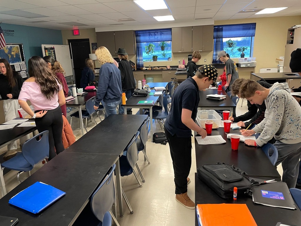 Students standing around tables in a classroom working on hands-on projects in groups