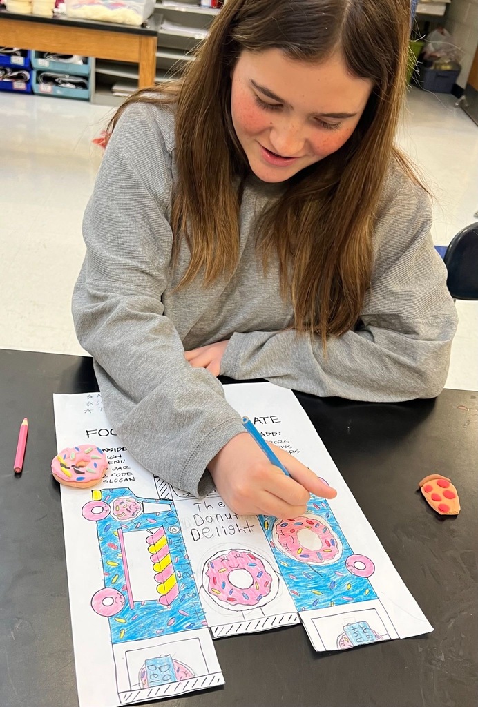 Students drawing on papers with colored pencils to bring their food trucks to life!
