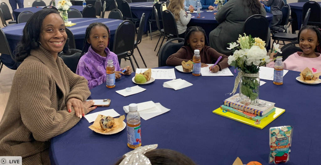 Families sitting around tables with breakfast items and coloring pages on the tables in front of them