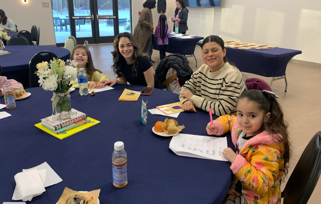 Families sitting around tables with breakfast items and coloring pages on the tables in front of them